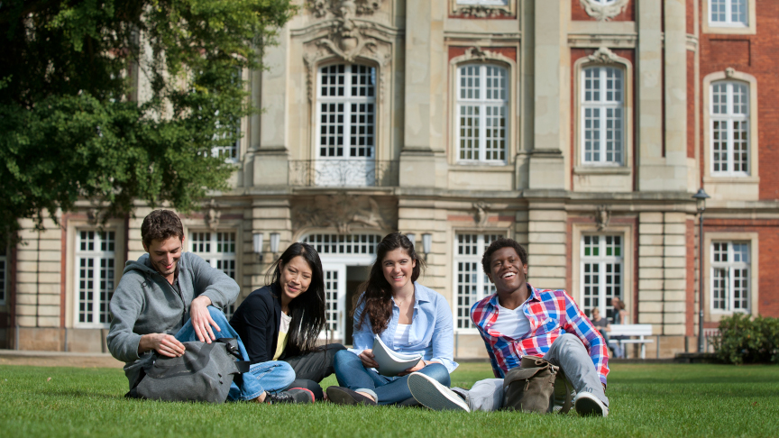International students sit on the lawn in front of the University of Bonn.